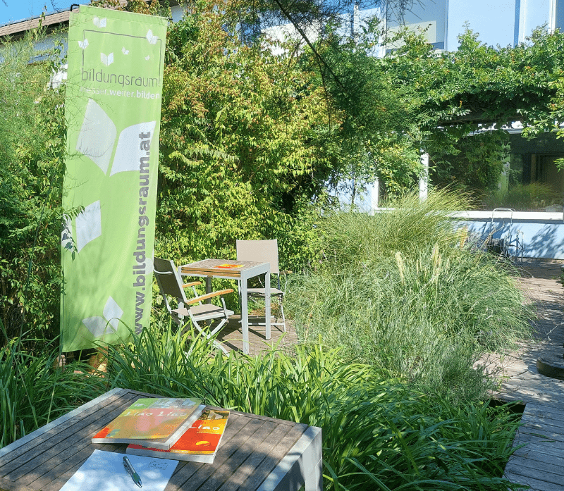 Lerngarten des Sprachenzentrums Bildungsraum. Mit Tisch, Sesseln und Lernmaterialien am Tisch.